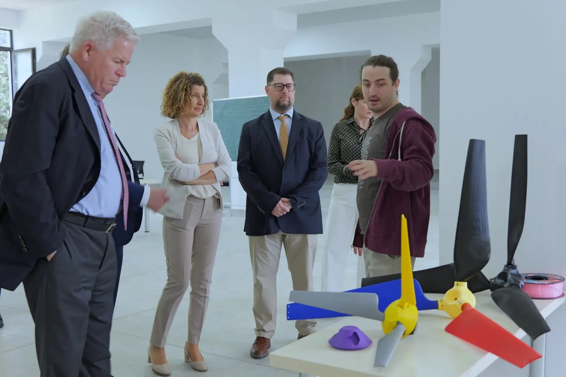 ფოტო, რომელზეც ანზორი კუპრაძე Horizon Europe-თან დაკავშირებულ სტუმრებს 3D ბეჭდვით დამზადებულ ქარის ტურბინის კომპონენტებს აცნობს.